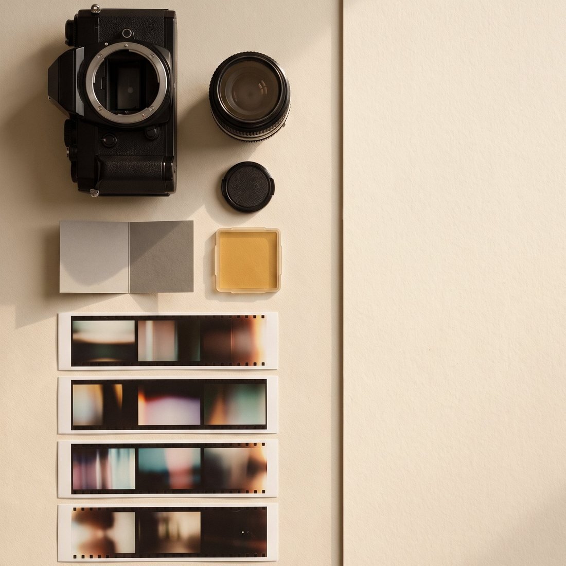 A camera body, lens, grey card, warm filter and four contact sheet strips laid out after a shoot